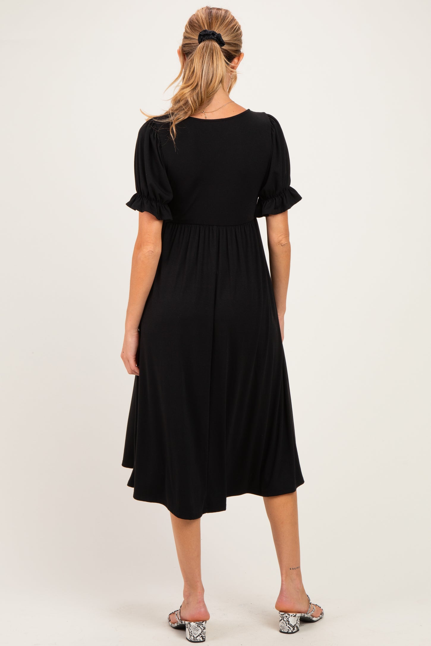 woman wearing a black maternity dress with short puff sleeves and a flowy skirt, showing her baby bump from the back