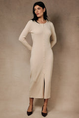 woman wearing a beige ribbed midi dress with buttons and a front slit, posing against a textured background
