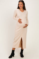 woman wearing a light beige ribbed maternity dress with a button front and slit, holding her baby bump