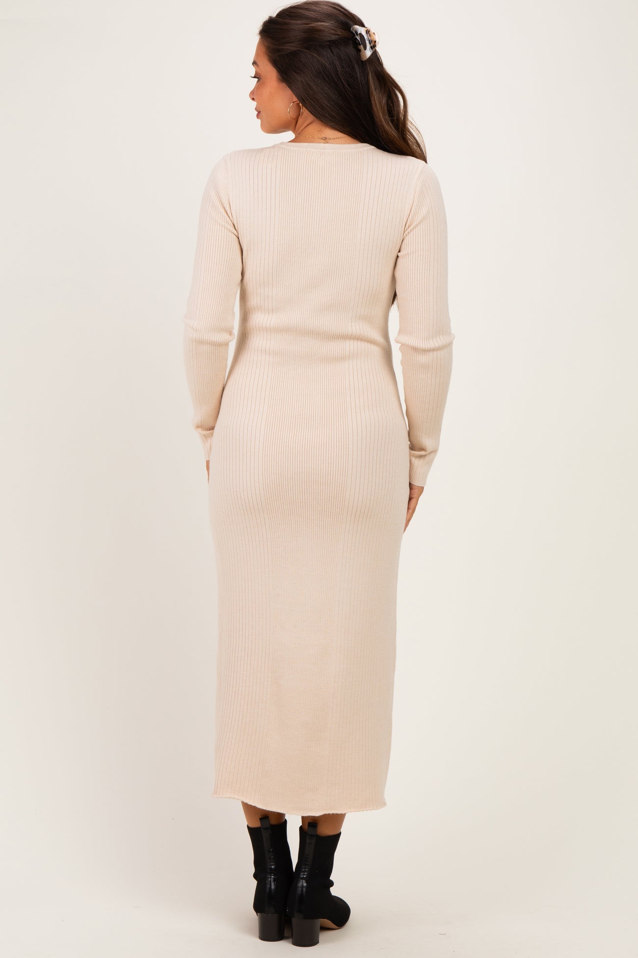 woman wearing a beige ribbed maternity dress with long sleeves, showing a fitted silhouette and midi length