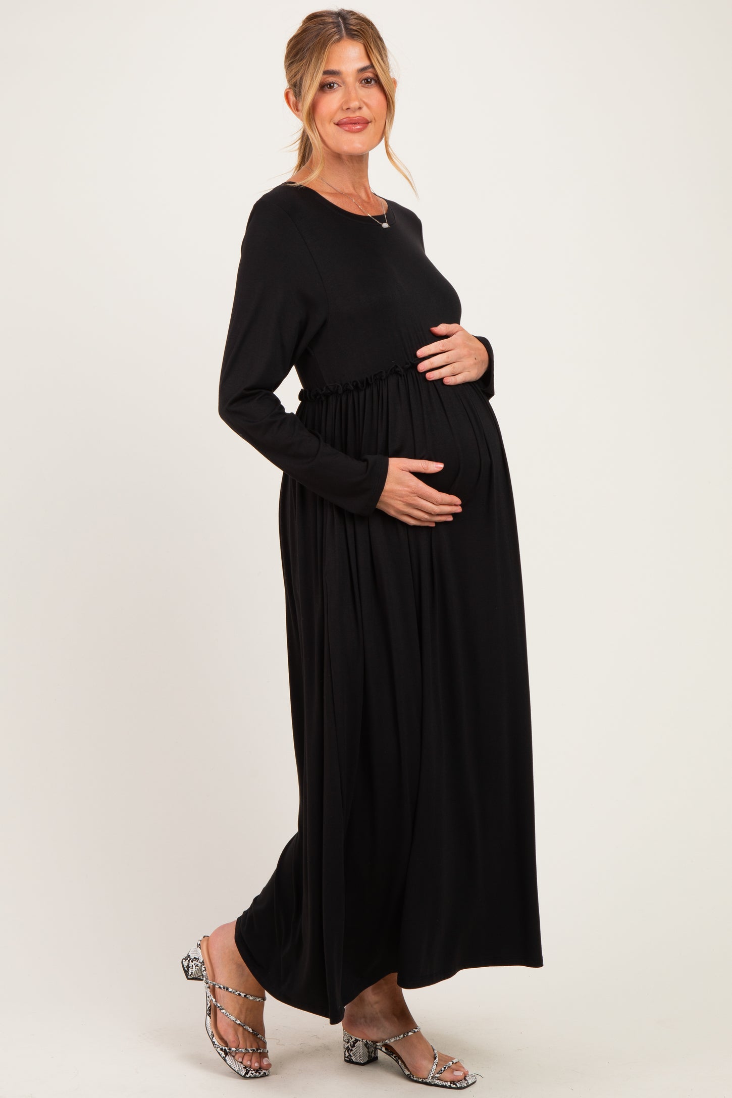 woman wearing a black long sleeve maternity dress with gathered waist, holding her baby bump