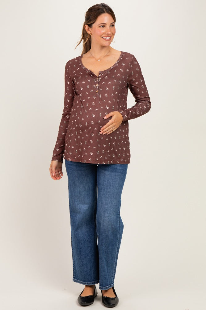 woman wearing a brown maternity long sleeve top with floral print and buttons, holding her baby bump, paired with blue jeans