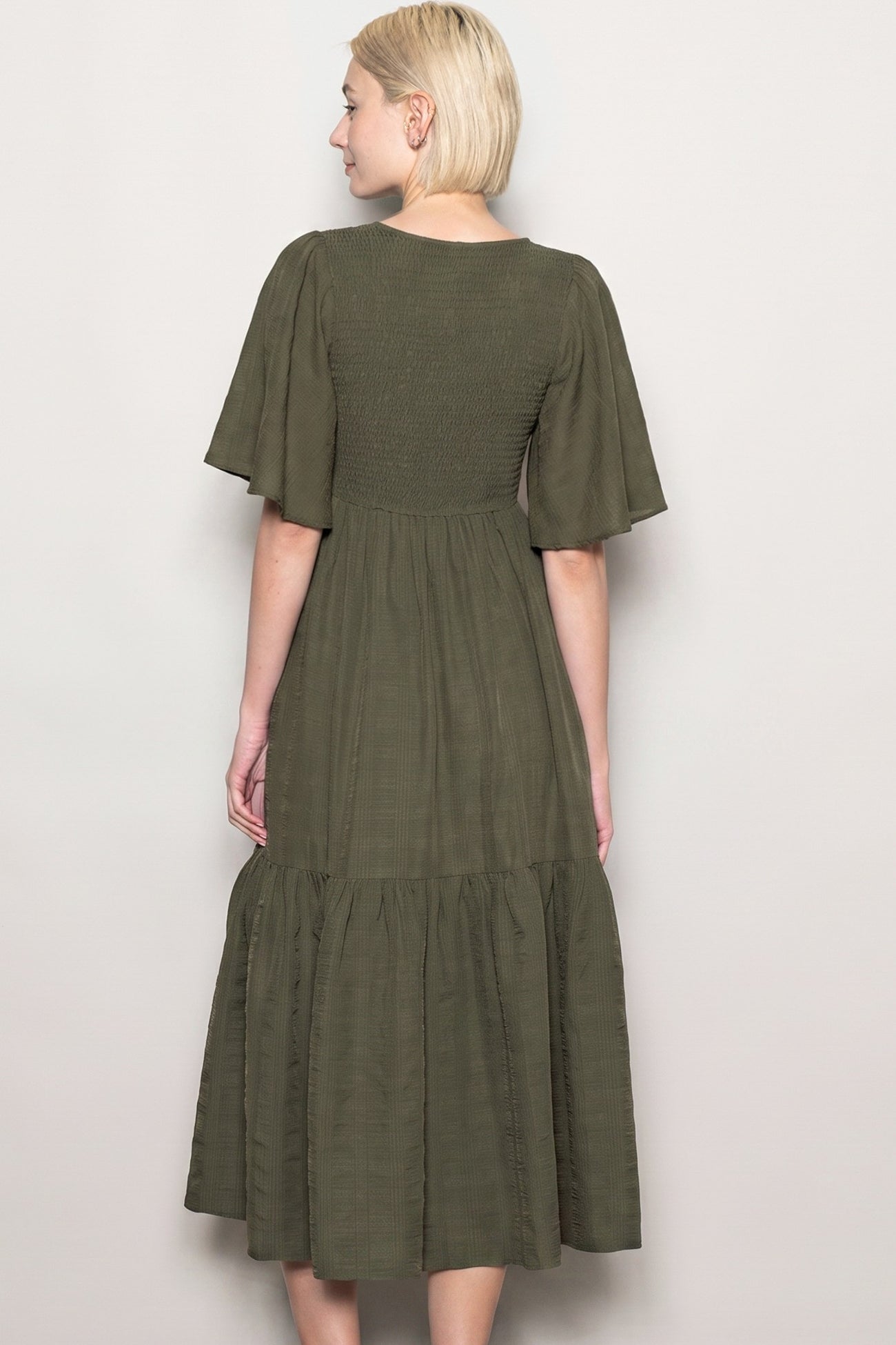woman wearing a dark green midi dress with short flutter sleeves and a tiered skirt, viewed from the back