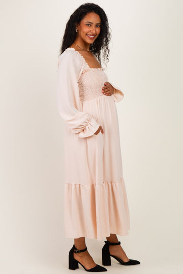 woman wearing a light pink maternity dress with a smocked bodice and long sleeves, touching her baby bump