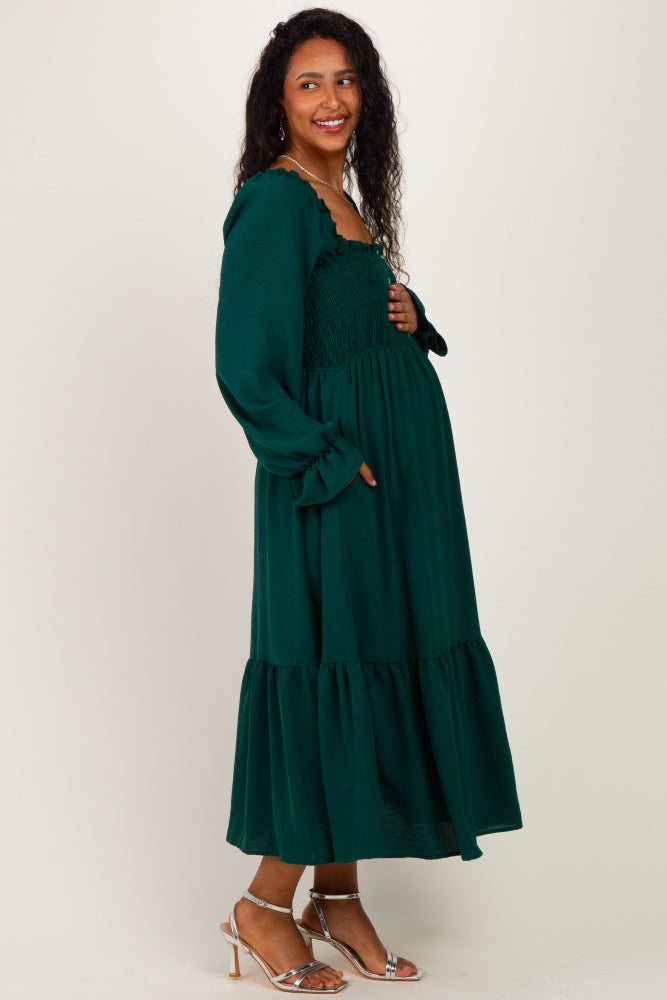 woman wearing a green maternity maxi dress with smocked bodice and tiered skirt, holding her baby bump