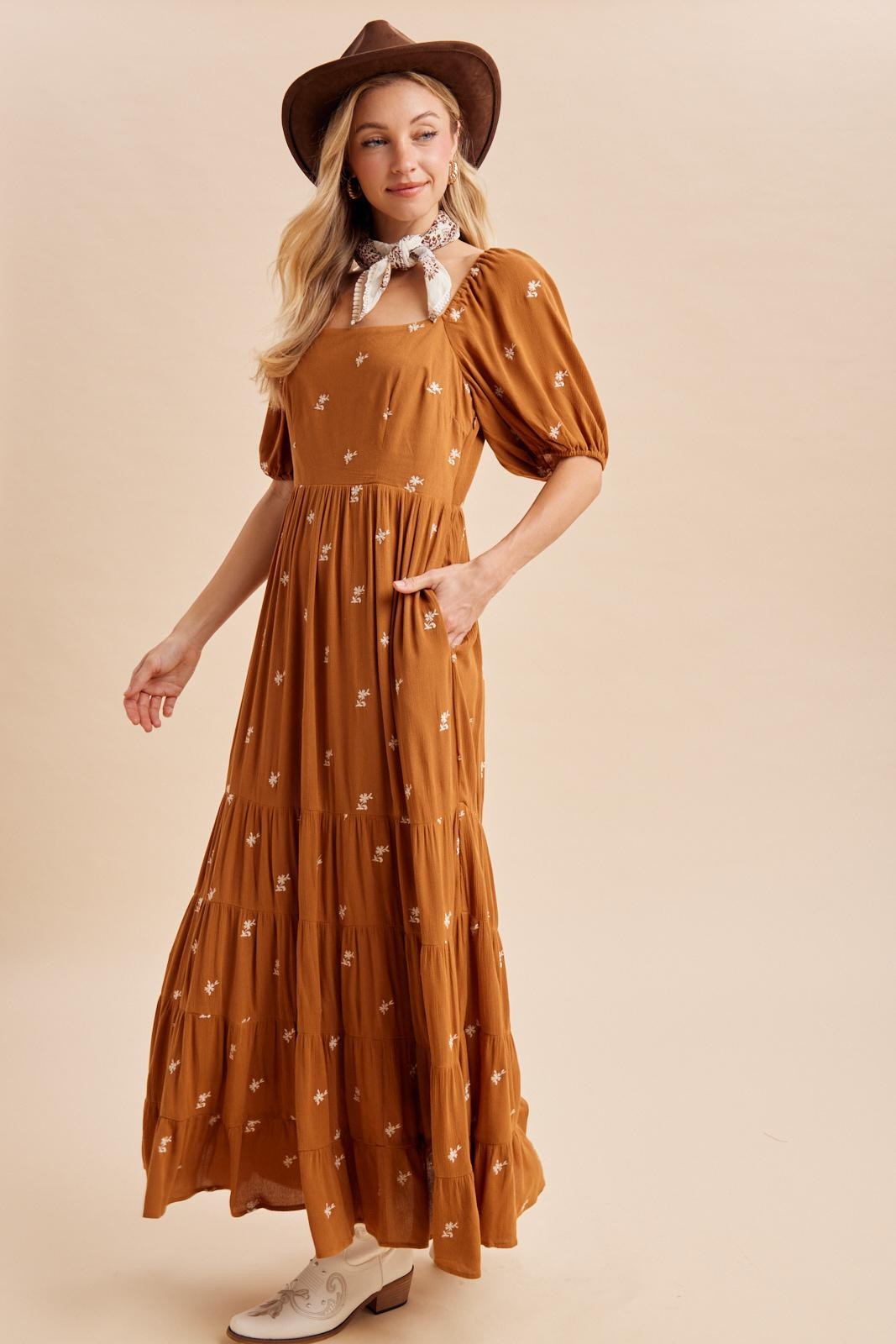 woman wearing a brown maxi dress with floral embroidery, puff sleeves, and a wide-brimmed hat