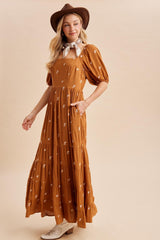 woman wearing a brown maxi dress with floral embroidery, puff sleeves, and a wide-brimmed hat