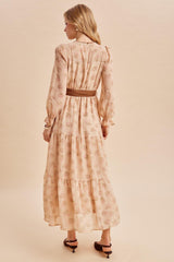 woman wearing a blush pink floral long sleeve maxi dress with a tiered skirt and a brown belt, viewed from the back
