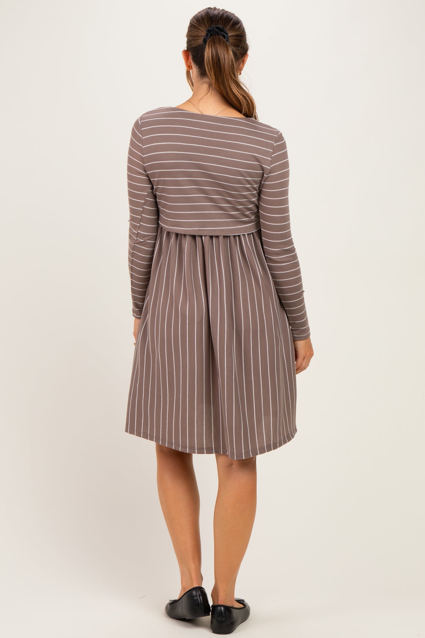woman wearing a brown striped maternity dress with long sleeves and a fitted bodice, showing a baby bump from the back