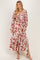 woman wearing a pink floral maxi dress with long sleeves and a square neckline, posing with one hand on her hip