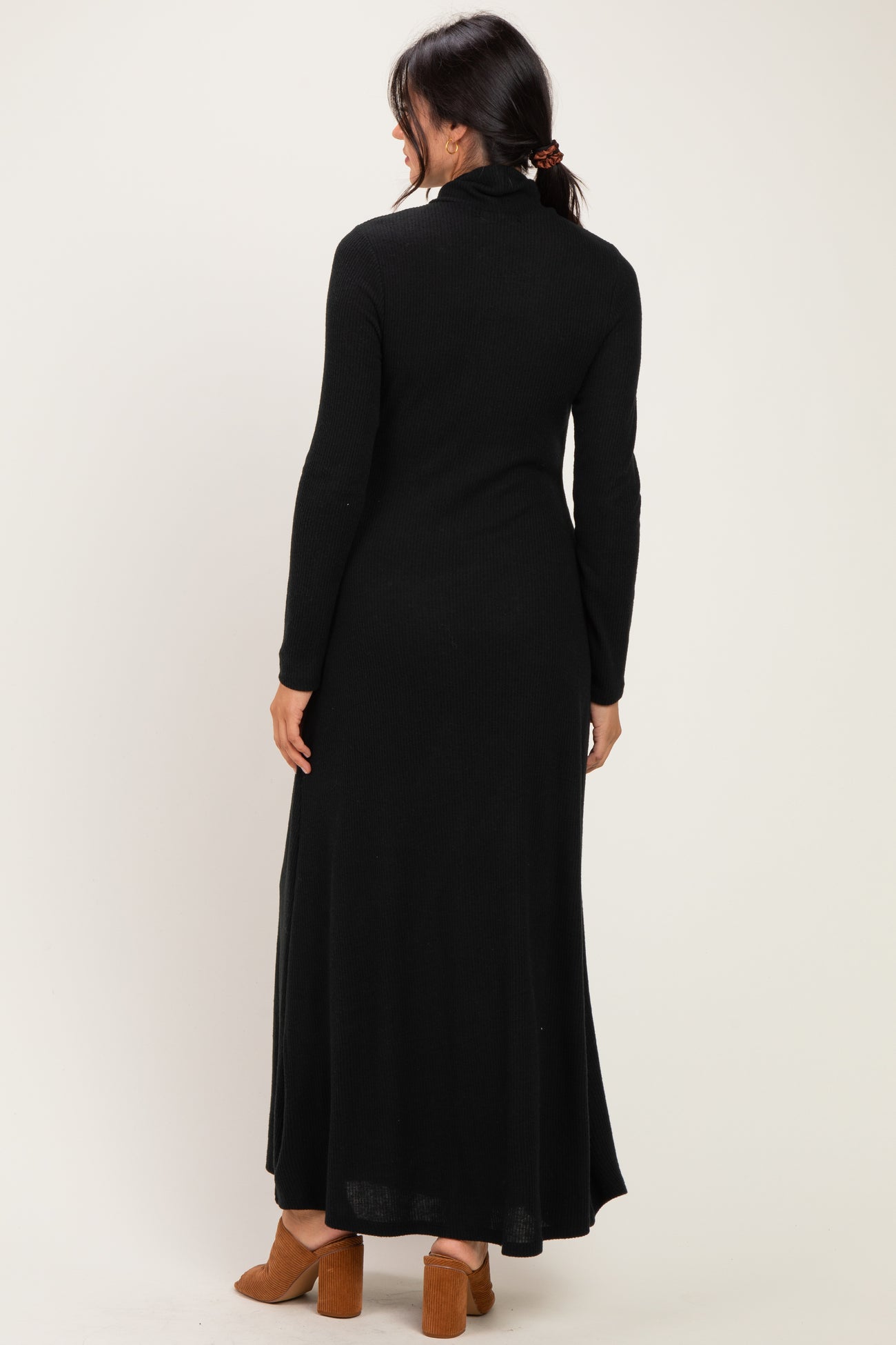 woman wearing a black long sleeve maxi dress with a high neckline and side slits, viewed from the back