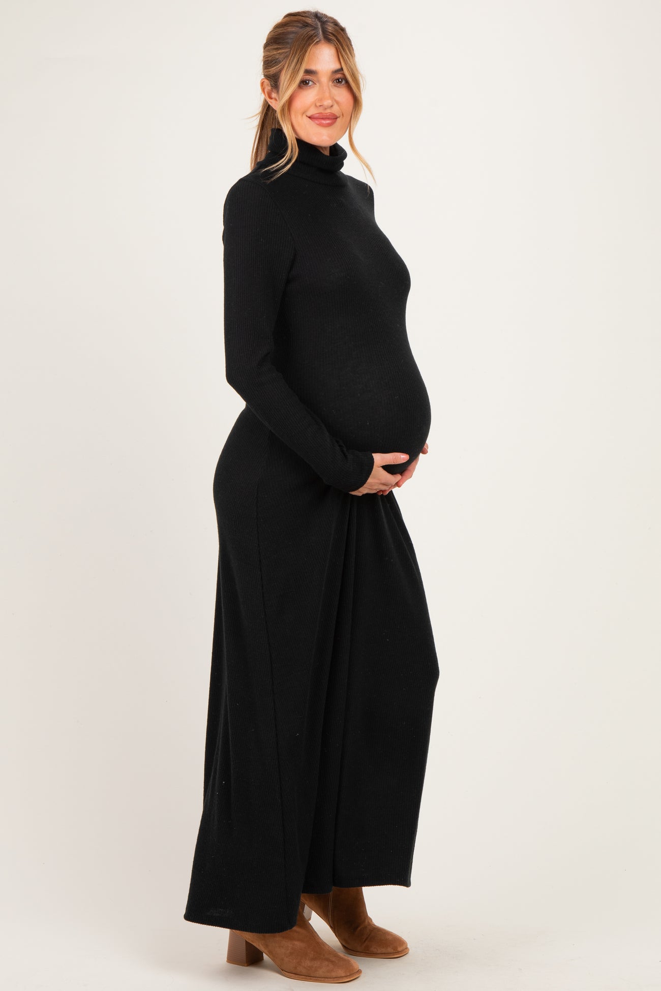 woman wearing a black long sleeve maternity dress with a high neckline and holding her baby bump