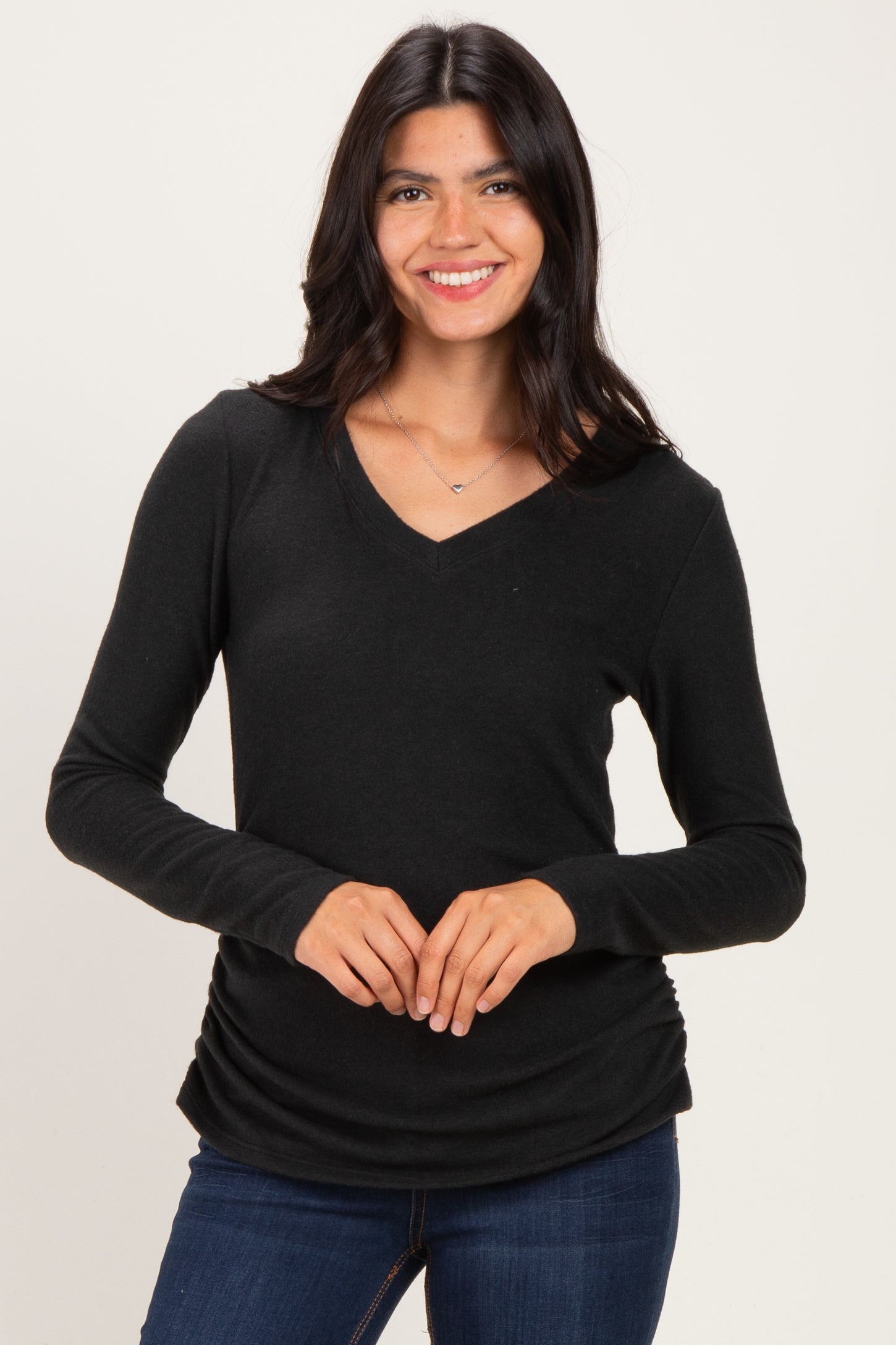 woman wearing a black long sleeve v-neck top with a gathered detail at the hem