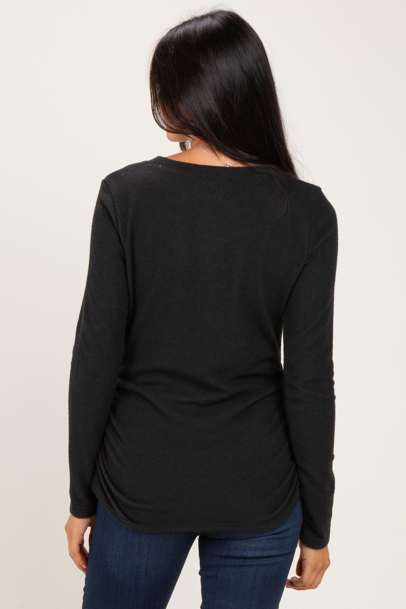 woman wearing a black long sleeve top with a scoop neck and gathered back detail, paired with blue jeans