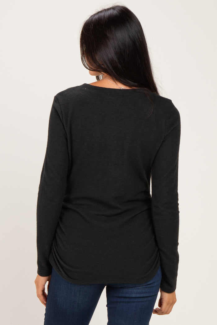 woman wearing a black long sleeve top with a scoop neck and gathered back detail, paired with blue jeans