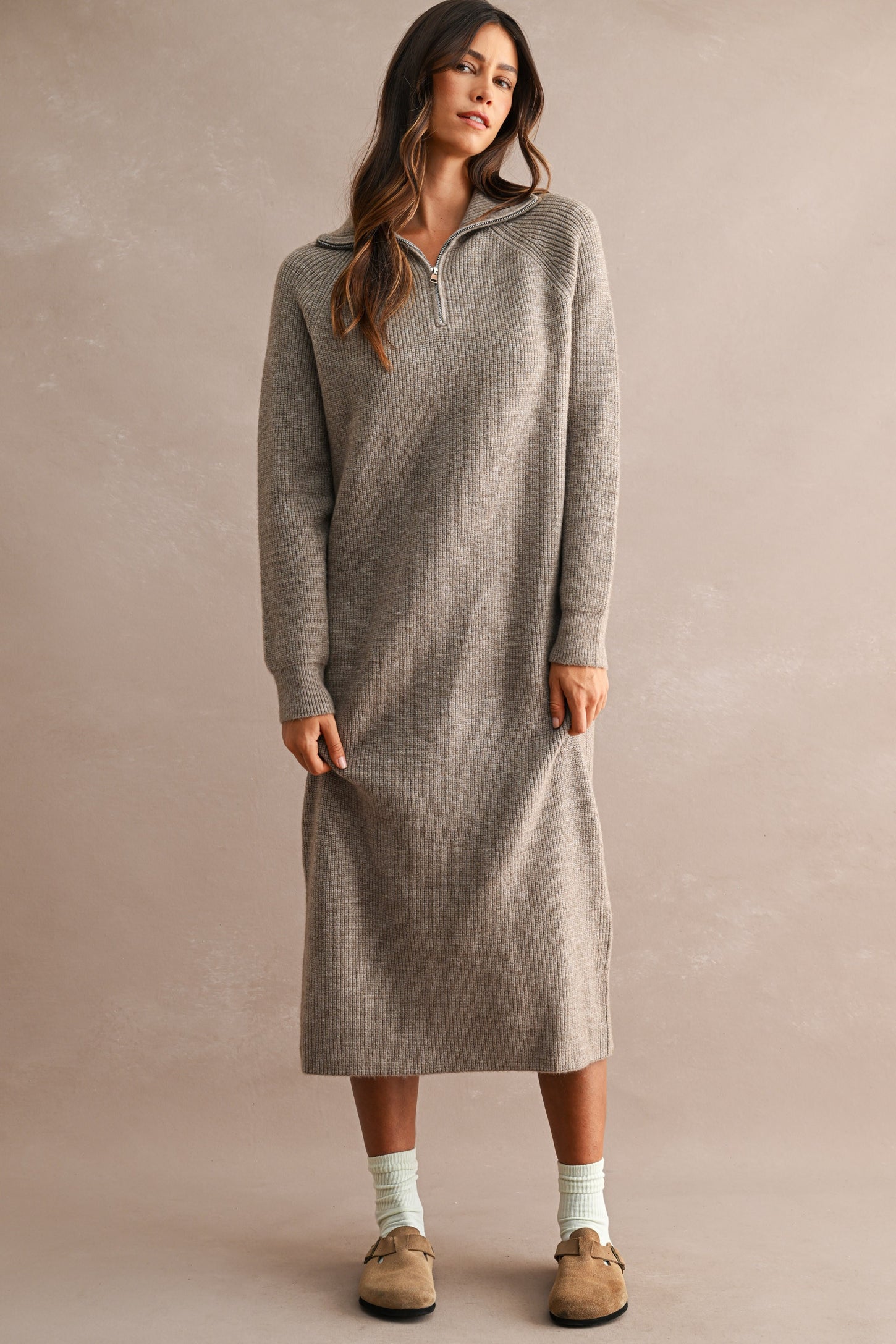 woman wearing a light gray ribbed knit long sleeve sweatshirt dress with a quarter zip and side slits