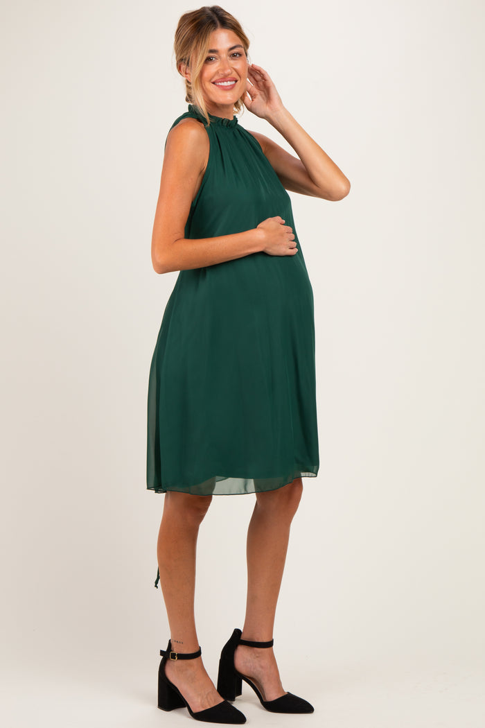 woman wearing a dark green sleeveless maternity dress with a high neckline and a baby bump visible