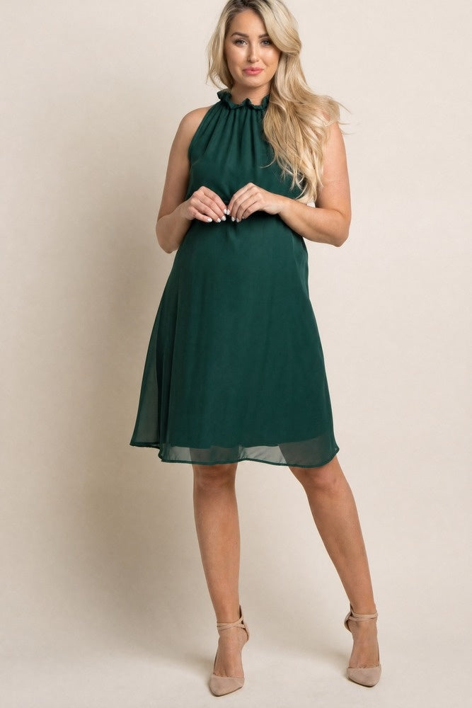woman wearing a dark green maternity dress with a ruffled neckline and a flowing silhouette, showing her baby bump