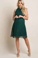 woman wearing a dark green maternity dress with a ruffled neckline and a flowing silhouette, showing her baby bump