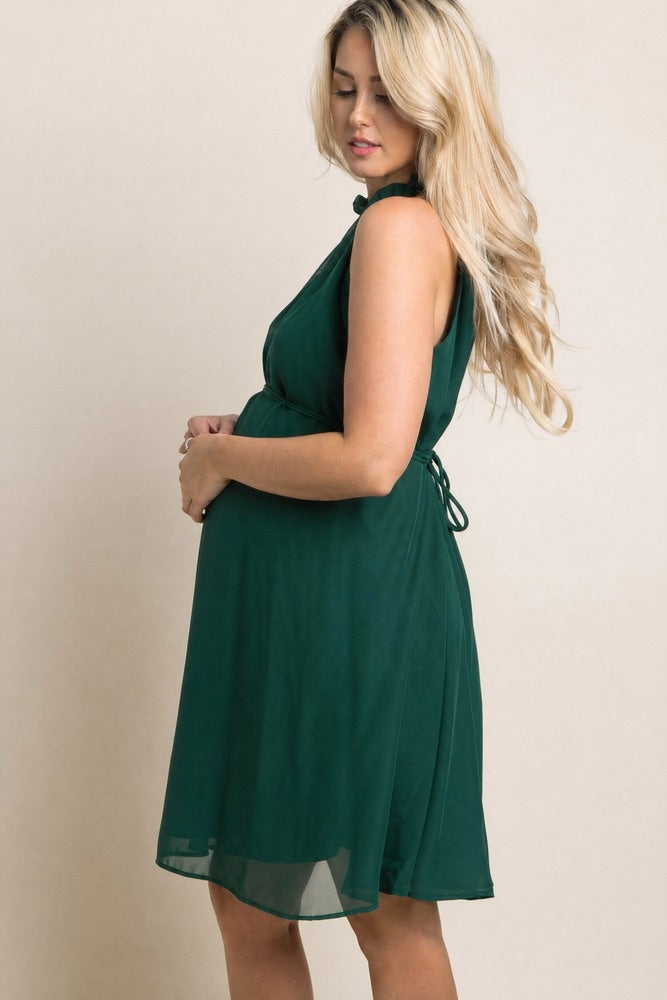 woman wearing a dark green maternity dress with a tie waist and ruffled neckline, showing baby bump from the side