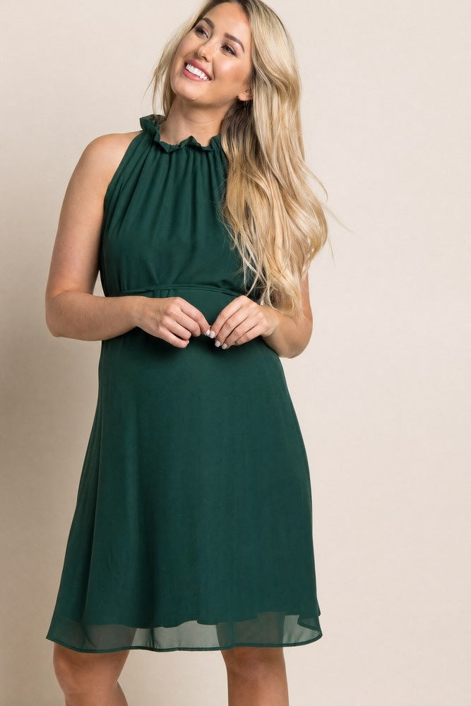 woman wearing a dark green maternity dress with a ruffled neckline and a flowing skirt, showcasing a baby bump