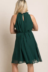 woman wearing a dark green maternity dress with a ruffled neckline and back keyhole detail, showing a baby bump