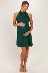 woman wearing a dark green maternity halter dress with a ruffled neckline and holding her baby bump