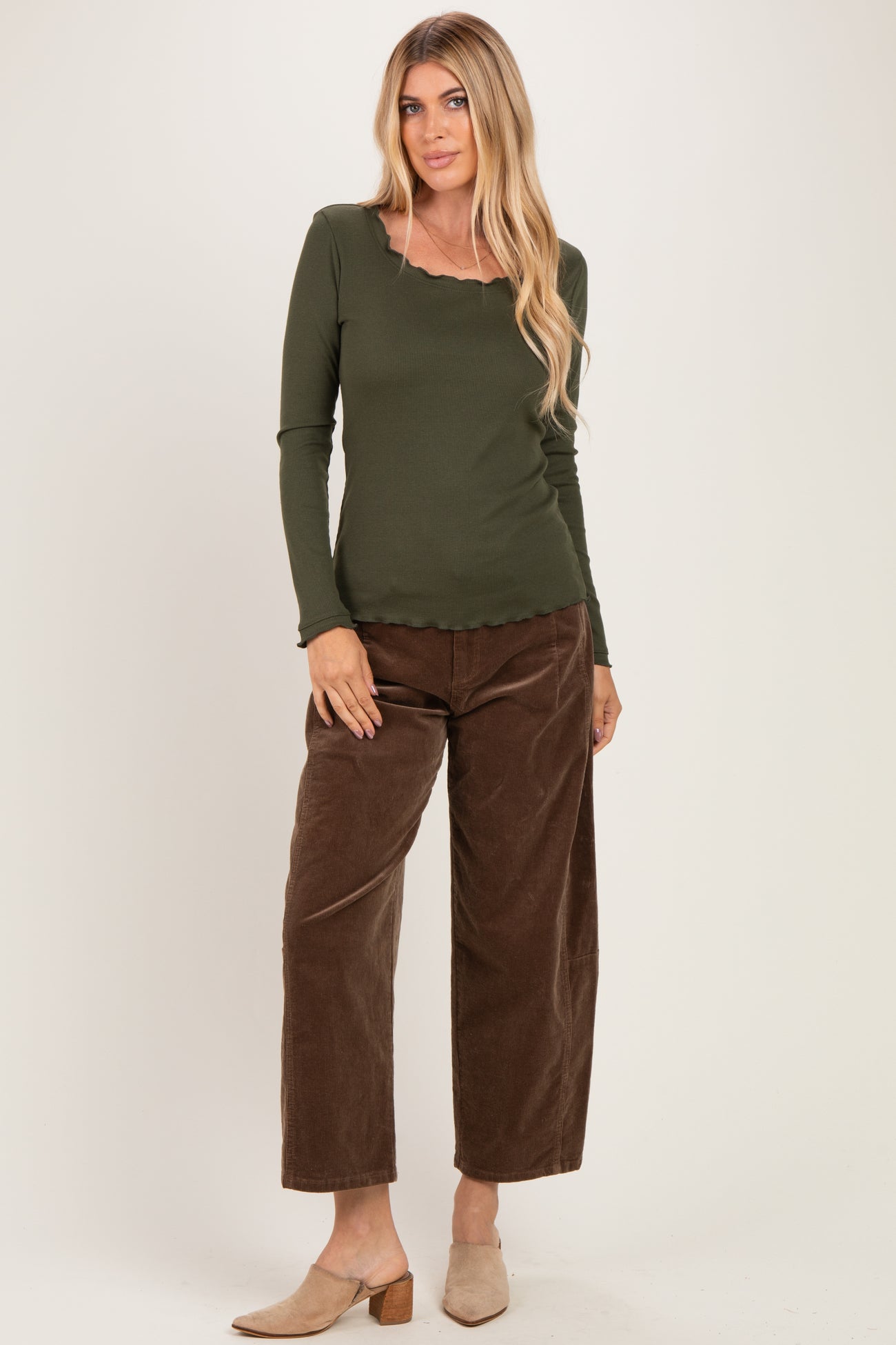 woman wearing an olive green long sleeve top with a scalloped neckline and brown wide-leg corduroy pants