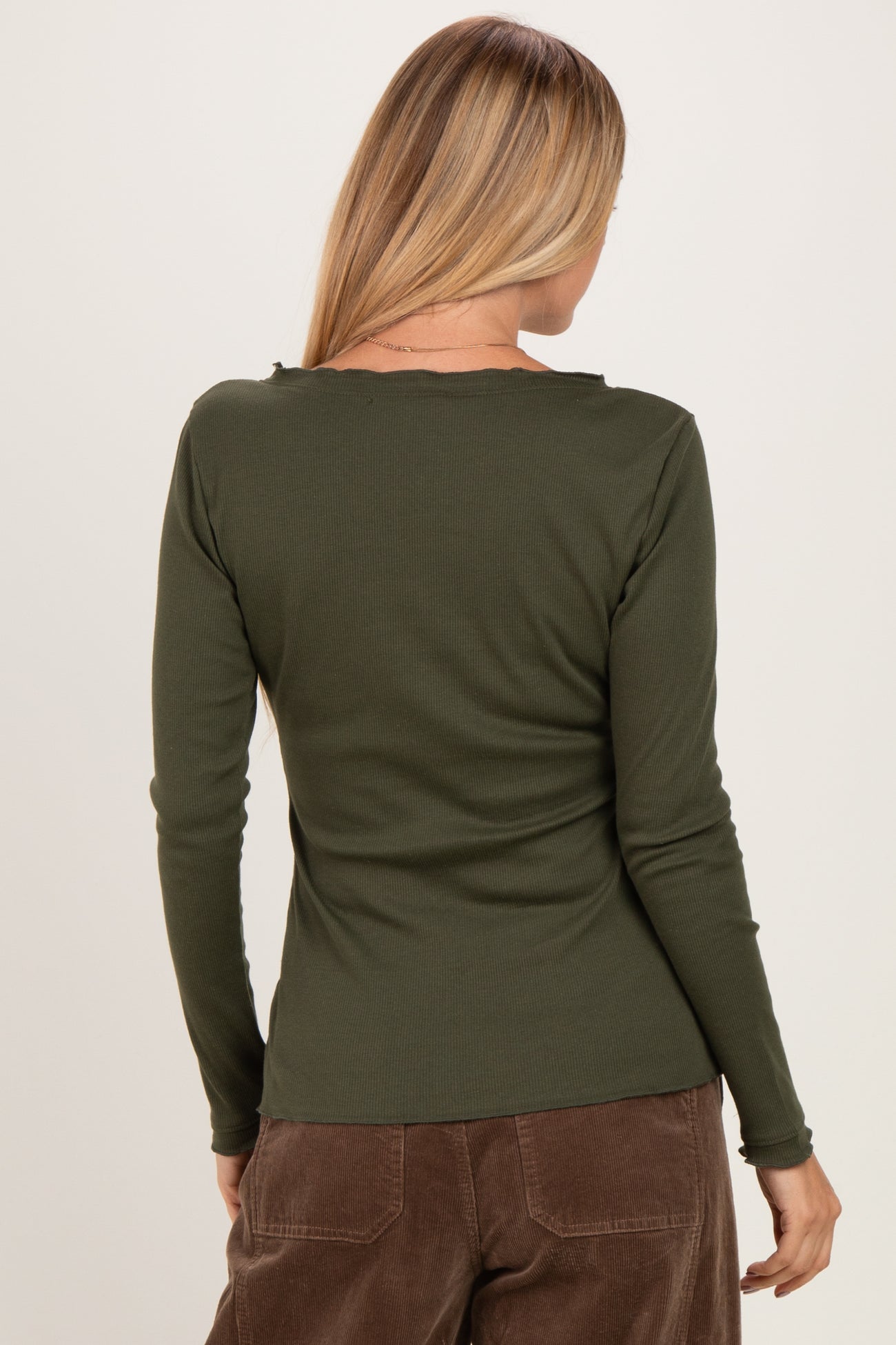 woman wearing a dark green long sleeve ribbed top, shown from the back