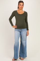 woman wearing a dark green maternity long sleeve top and light blue flared jeans, with a visible baby bump