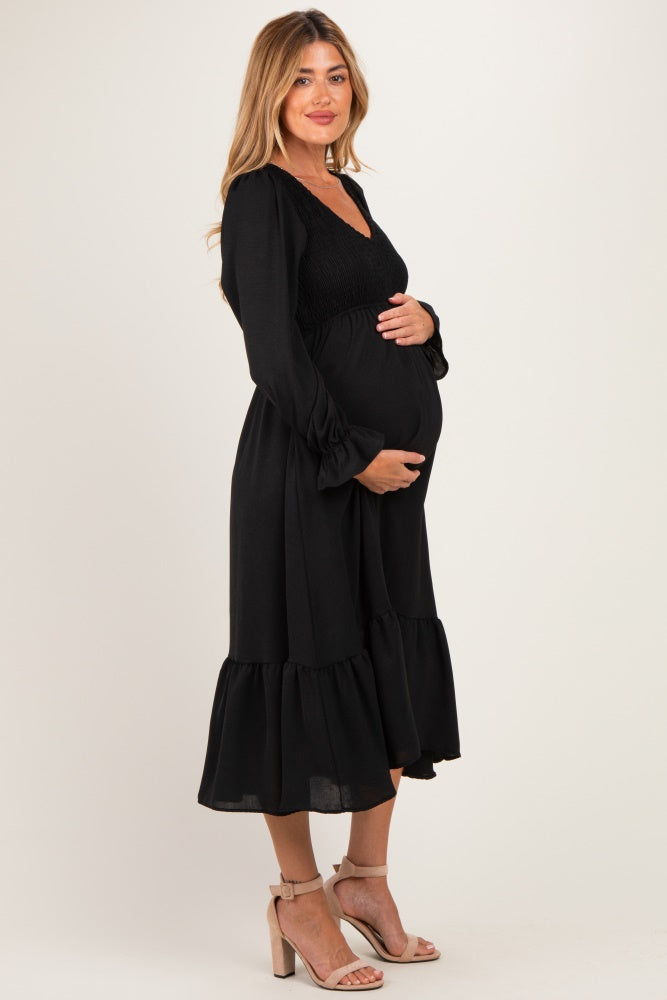 woman wearing a black maternity dress with a smocked bodice and ruffled hem, gently cradling her baby bump