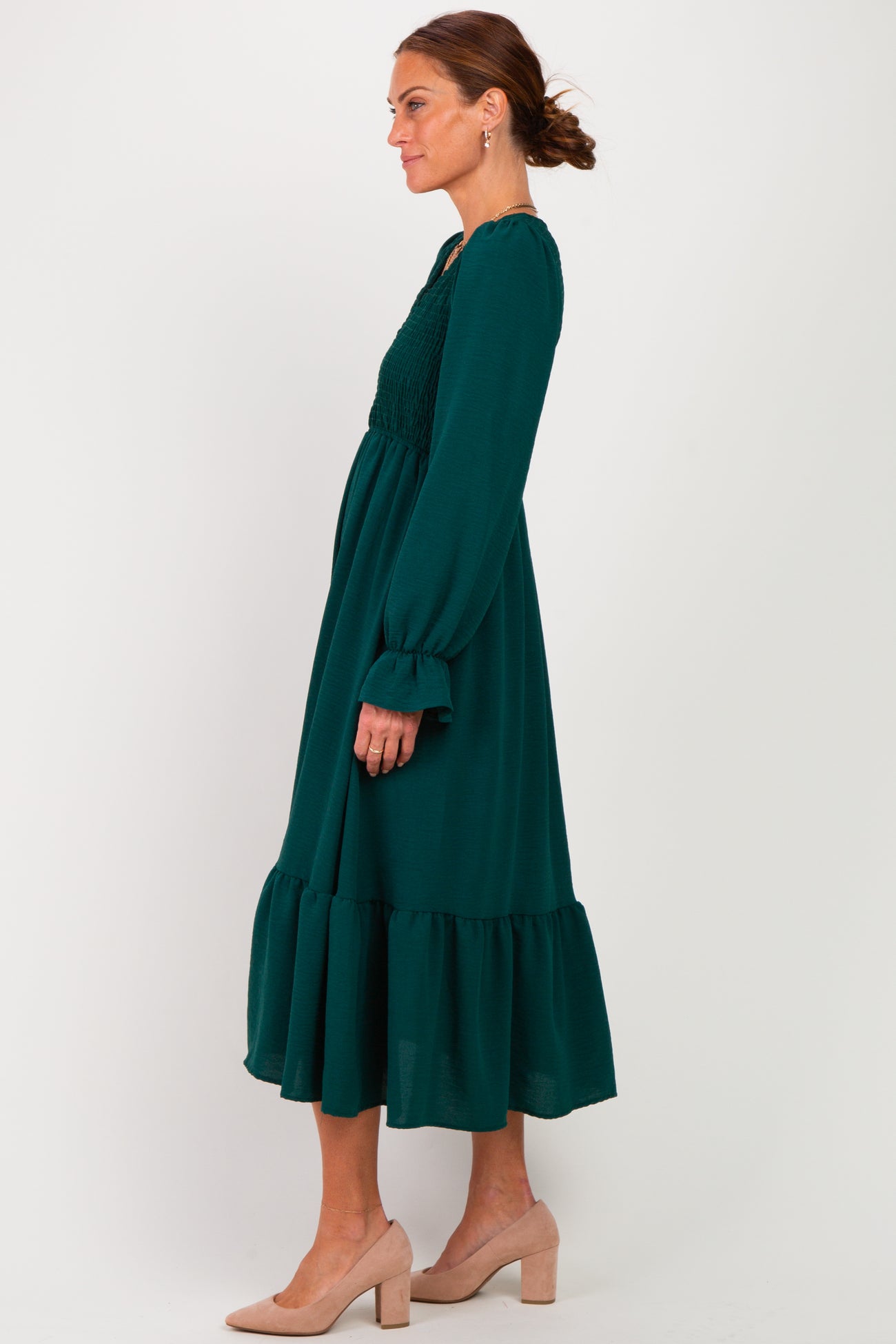 woman wearing a dark green long sleeve maxi dress with smocked bodice and ruffled hem, styled with nude heels