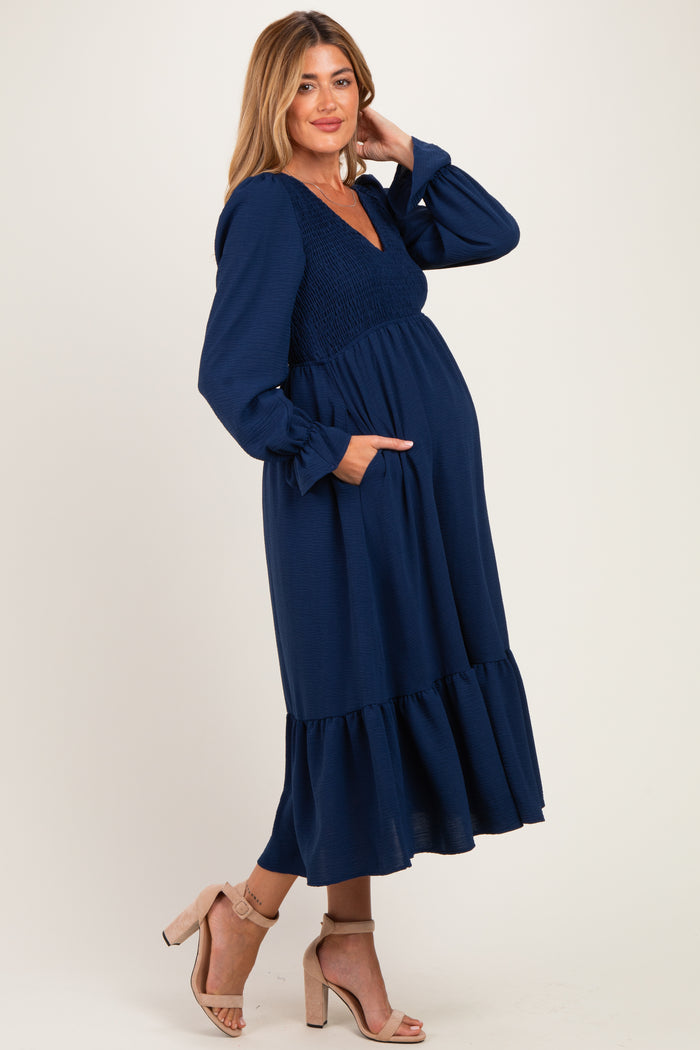 woman wearing a navy blue maternity dress with long sleeves, smocked bodice, and tiered skirt, showcasing her baby bump