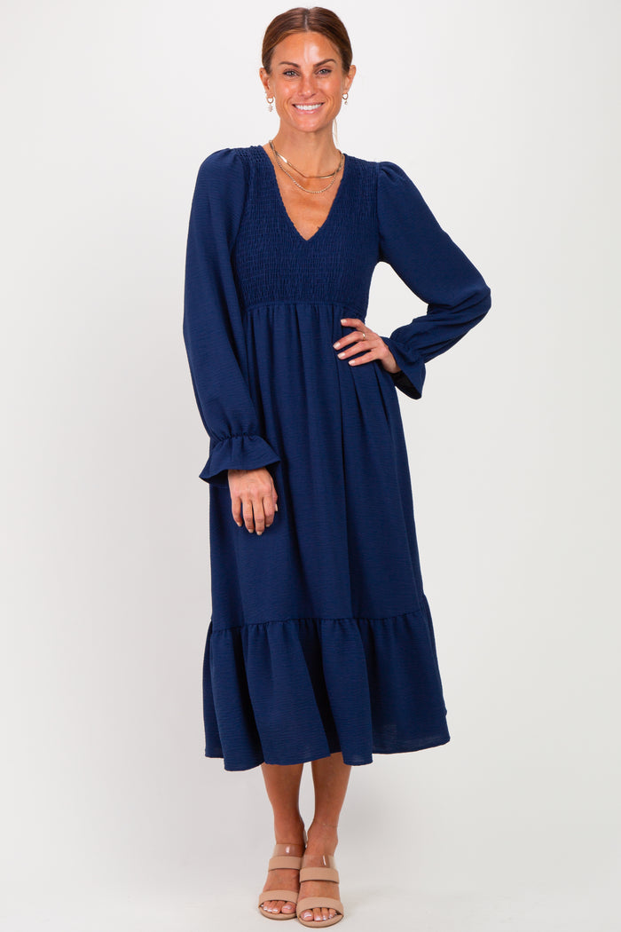 woman wearing a navy blue long sleeve tiered midi dress with a smocked bodice and ruffled hem, smiling at the camera
