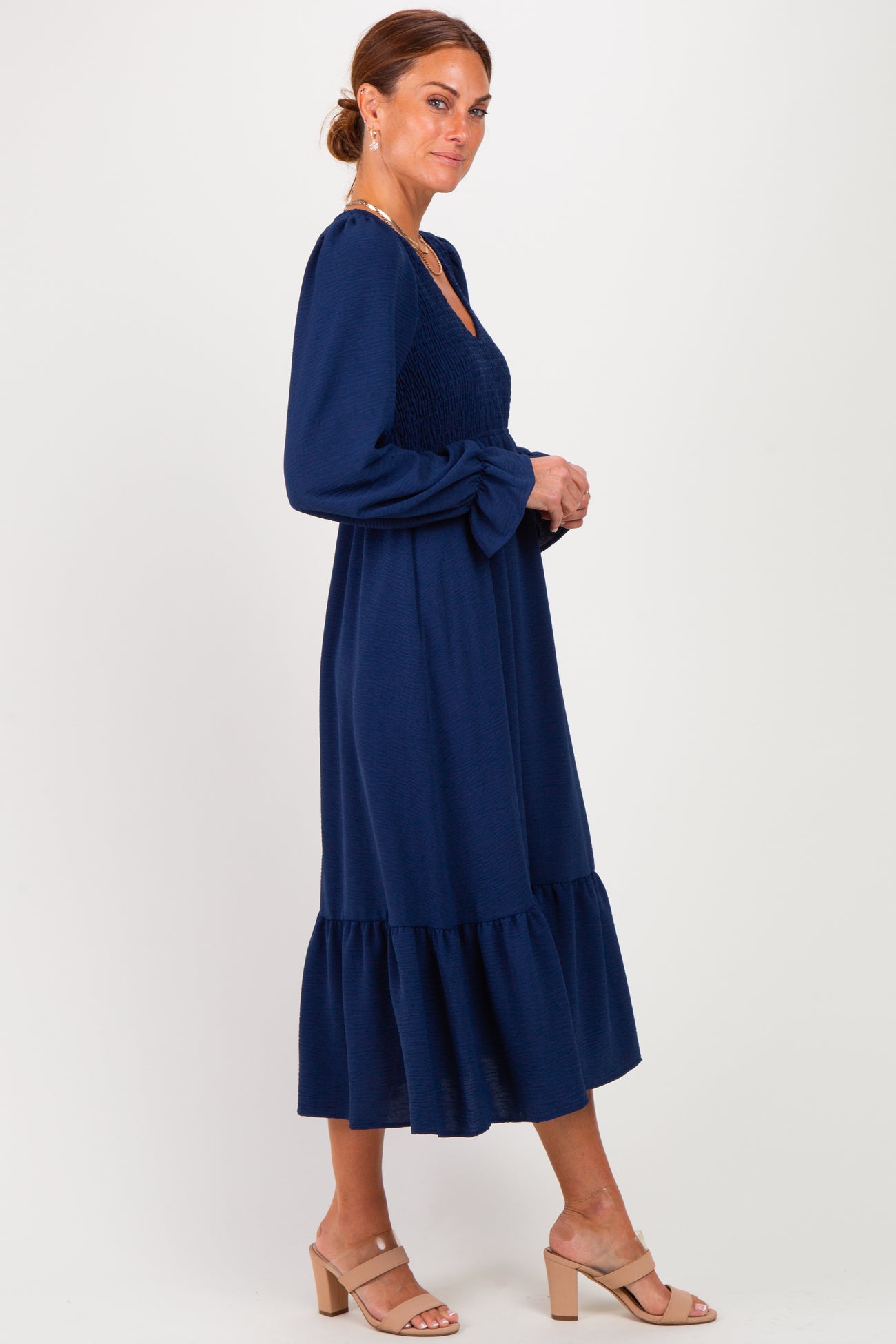 woman wearing a navy blue long sleeve dress with a smocked bodice and tiered ruffle hem, standing sideways