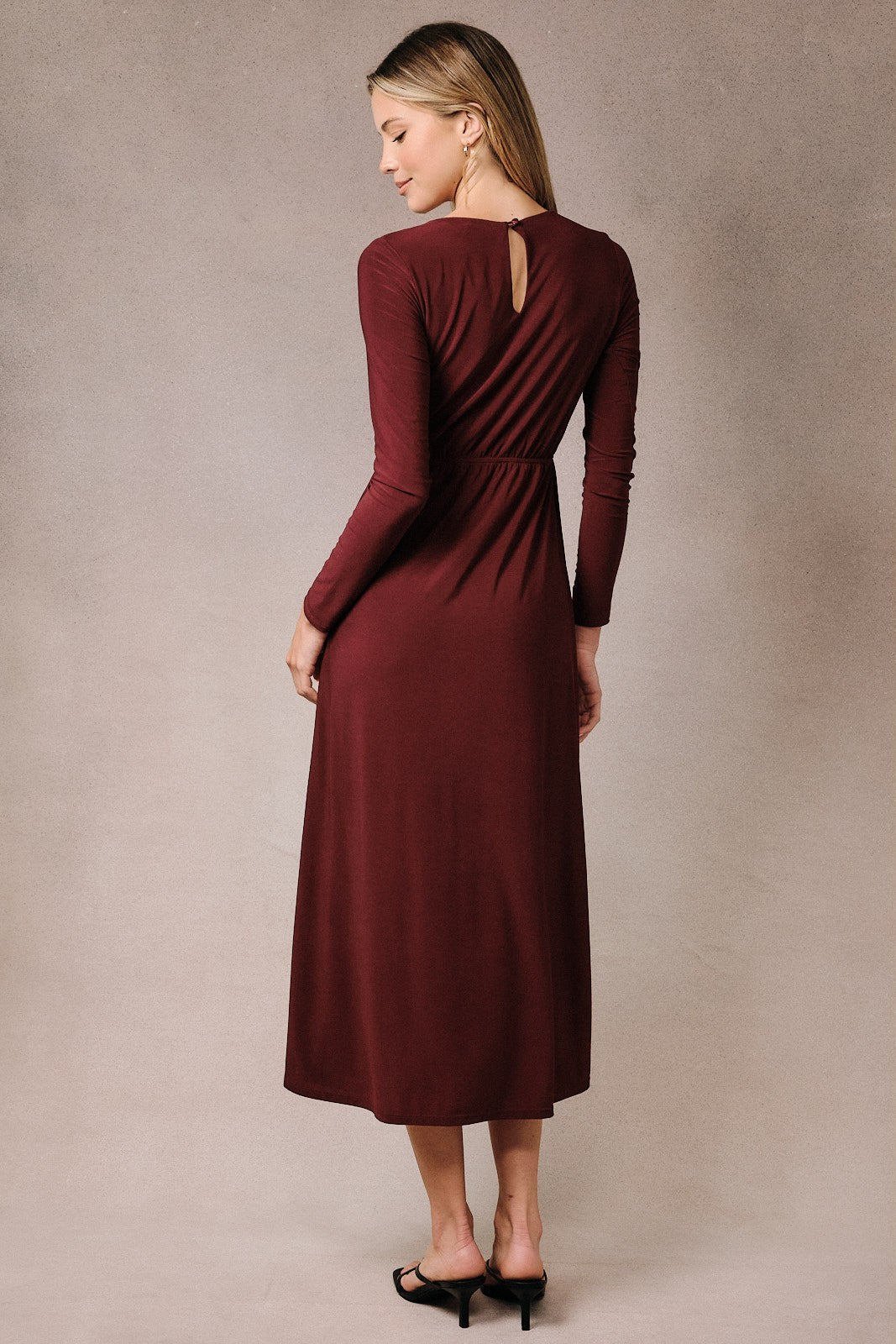 woman wearing a burgundy long sleeve midi dress with a keyhole back and gathered waist, viewed from the back