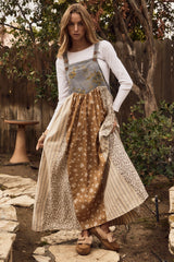 woman wearing a long patchwork dress with floral and striped patterns over a white long sleeve top and wooden sandals