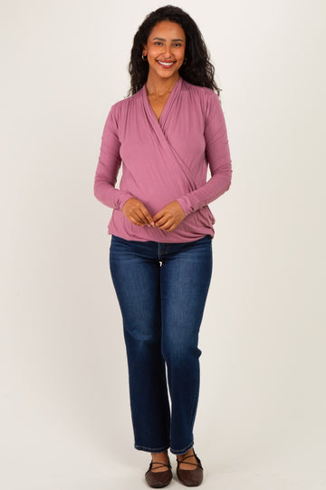 woman wearing a mauve long sleeve wrap maternity top and blue jeans, smiling with her hands together