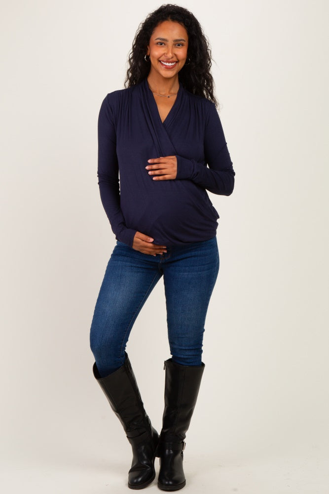 woman wearing a navy blue long sleeve maternity top and holding her baby bump while standing in skinny jeans and black boots