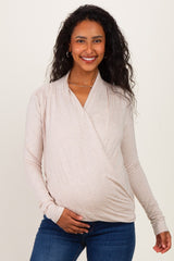 woman wearing a light beige maternity wrap top and holding her baby bump with a smile