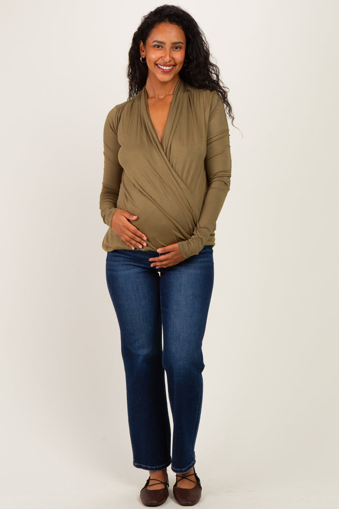 woman wearing an olive green wrap maternity top and blue jeans, cradling her baby bump