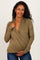 woman wearing a light olive green maternity wrap top, gently holding her baby bump with a smile