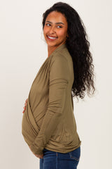 woman wearing an olive green wrap maternity top and holding her baby bump