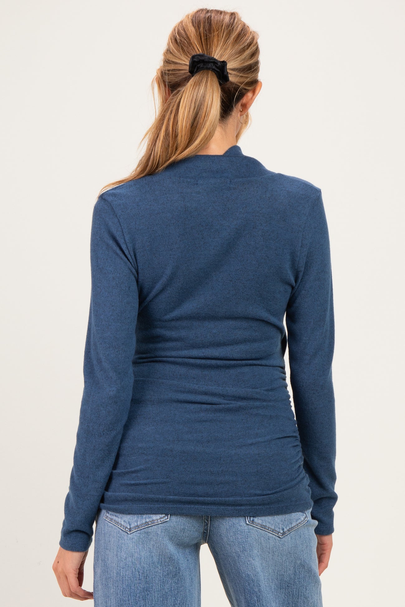 woman wearing a dark blue long sleeve maternity top, seen from the back, paired with light wash jeans