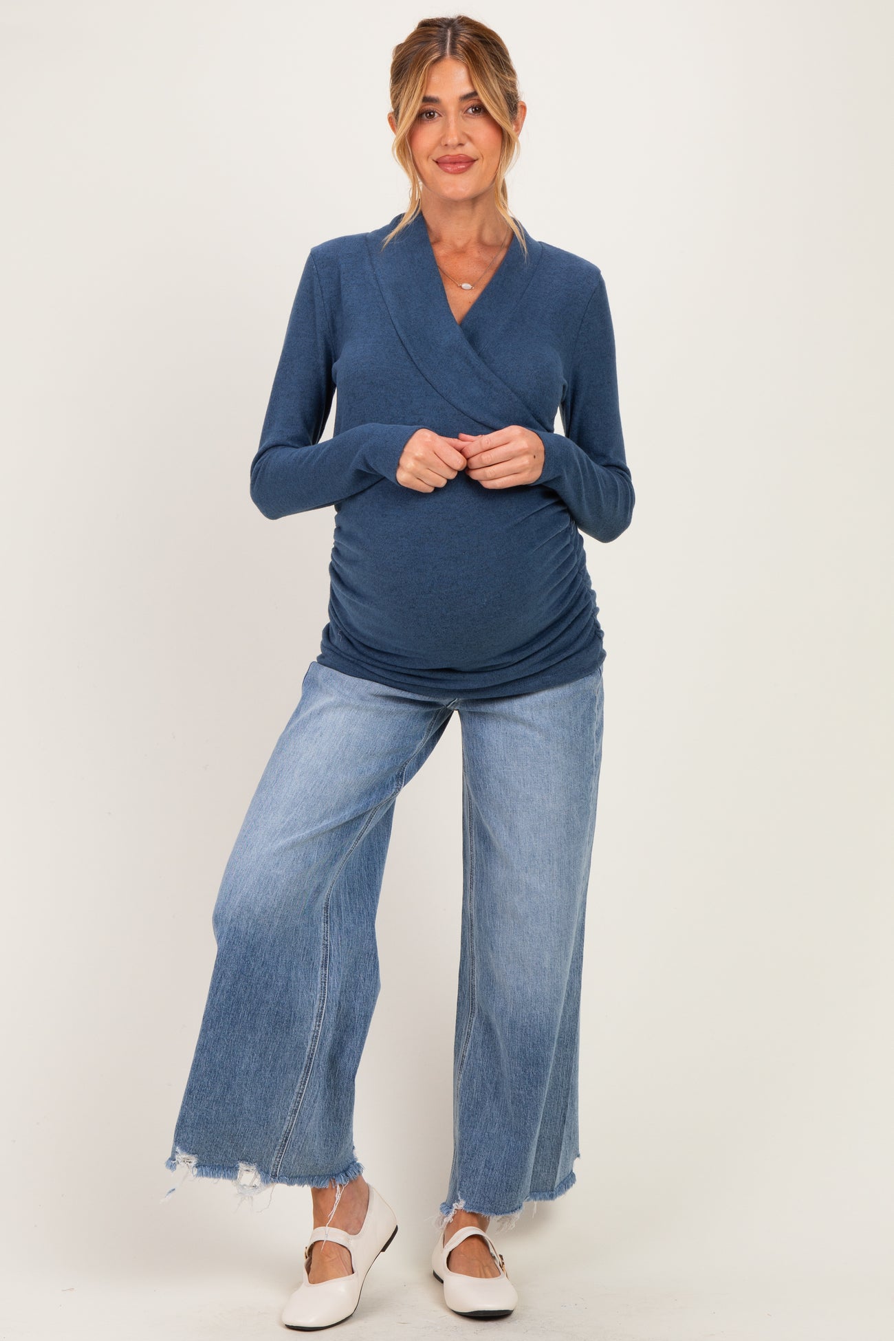 woman wearing a navy blue long sleeve maternity top that highlights her baby bump, paired with wide leg distressed jeans