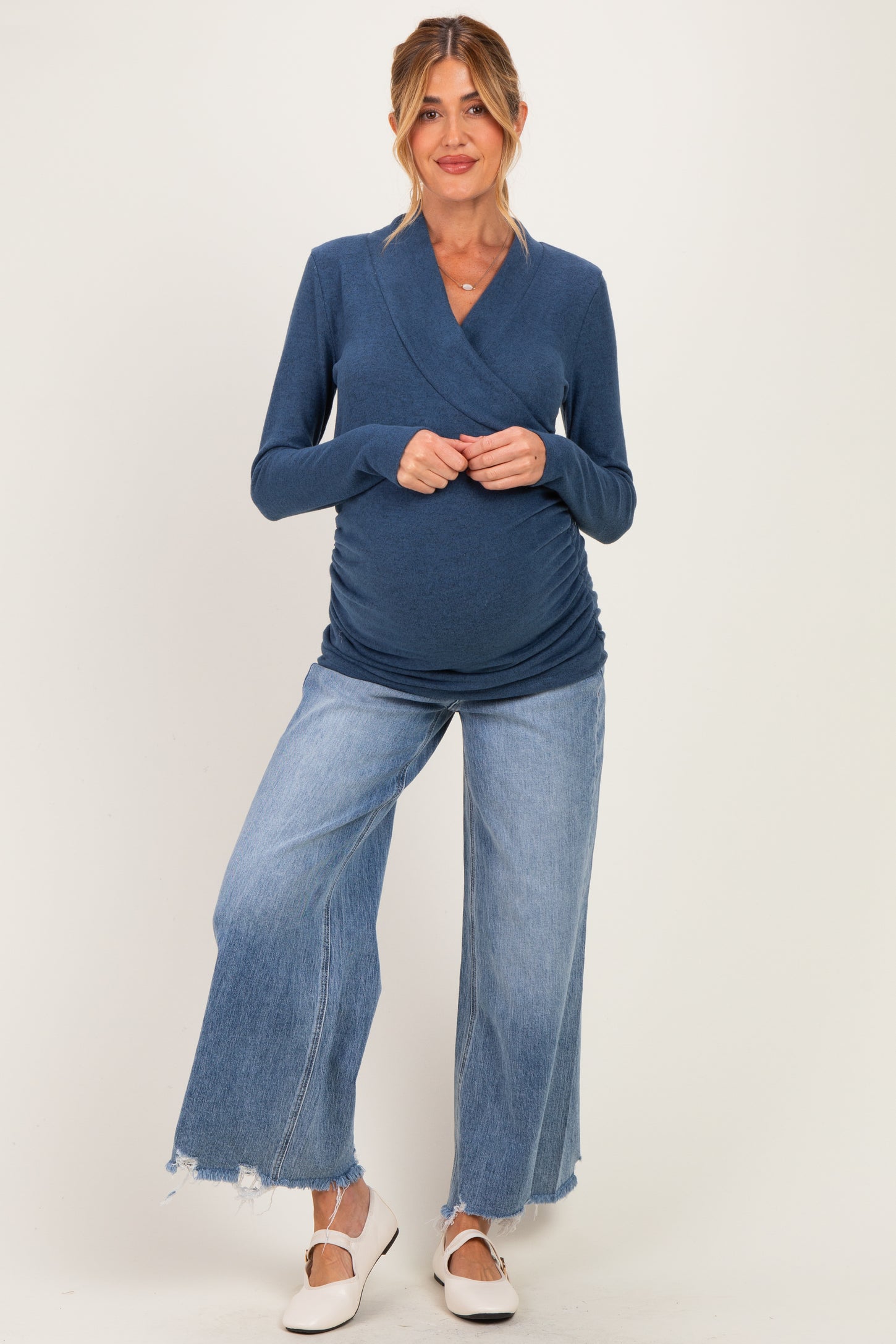 woman wearing a navy blue long sleeve maternity top that highlights her baby bump, paired with wide leg distressed jeans