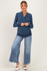 woman wearing a navy blue long sleeve maternity top that highlights her baby bump, paired with wide leg distressed jeans