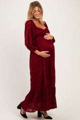 woman wearing a burgundy lace maternity dress with long sleeves and a ruffled hem, holding her baby bump