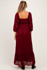 woman wearing a burgundy lace maternity maxi dress with three-quarter sleeves and a ruffled hemline