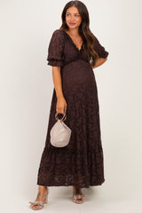 woman wearing a brown lace maternity dress with puff sleeves and a flowy skirt, holding a small handbag and showing her baby bump